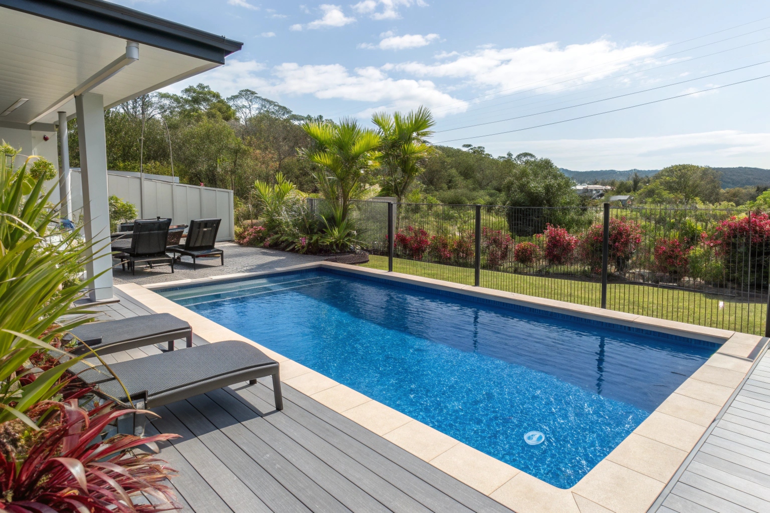 Modern composite pool deck surrounding a sparkling blue residential pool in a sunny Queensland backyard, with outdoor furniture and lush coastal garden